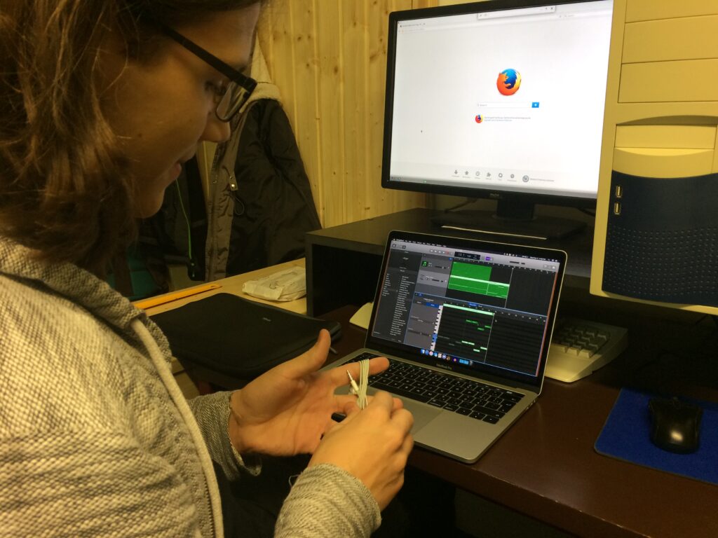 Kluk motá sluchátka a před sebou má notebook se softwarem pro editaci hudby a monitor zobrazující prohlížeč Firefox.