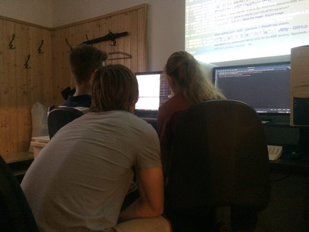Tři studenti koukají na společně na zdrojový kód v počítači.
