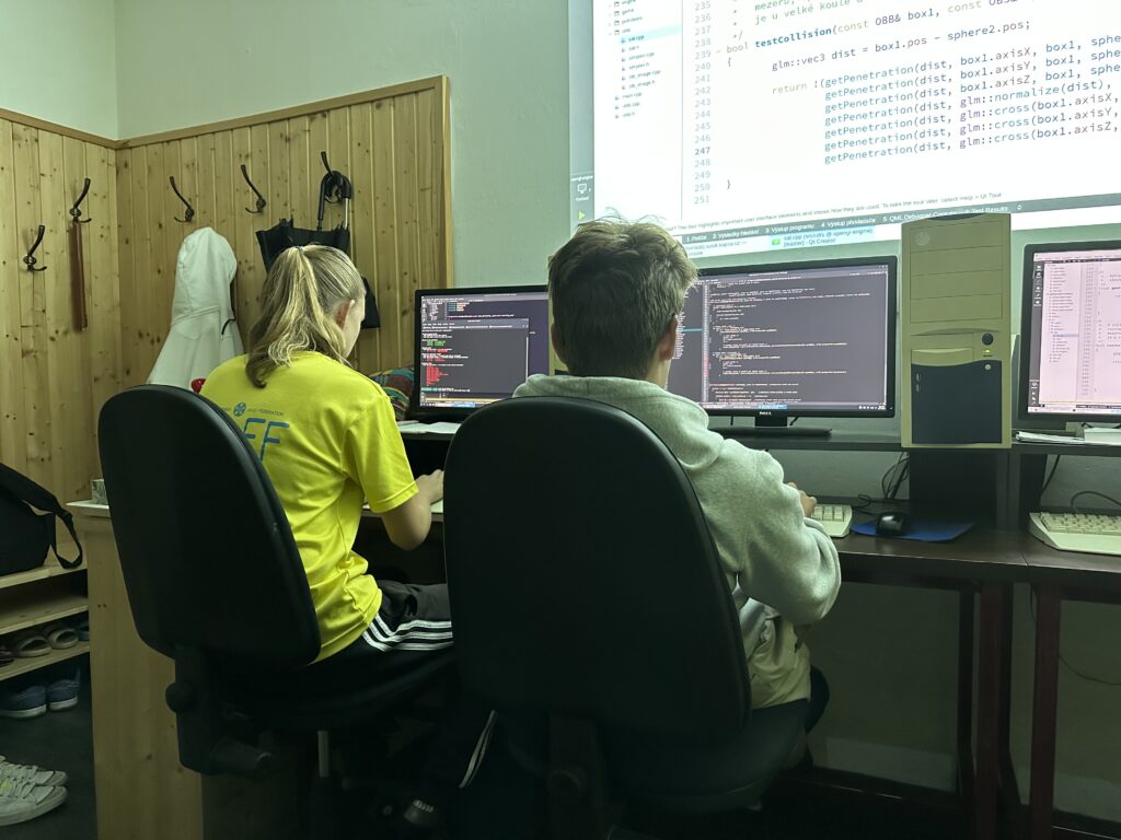 Studentka pracuje s gitem, student příše programový kód pro detekci kolizí.