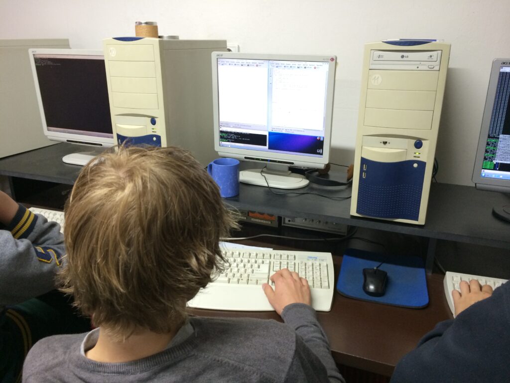 Děti píšící na klávesnici u stolu s více monitory a počítači.