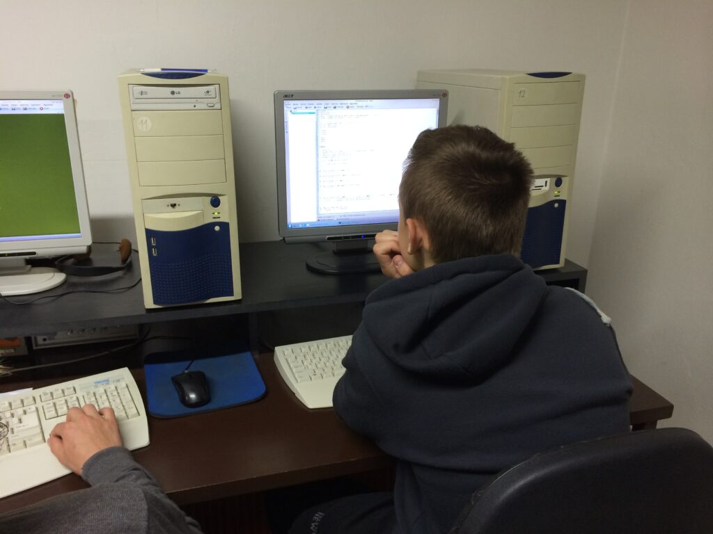 Dva lidé pracují na počítačích s více monitory, počítačovými skříněmi a klávesnicemi.