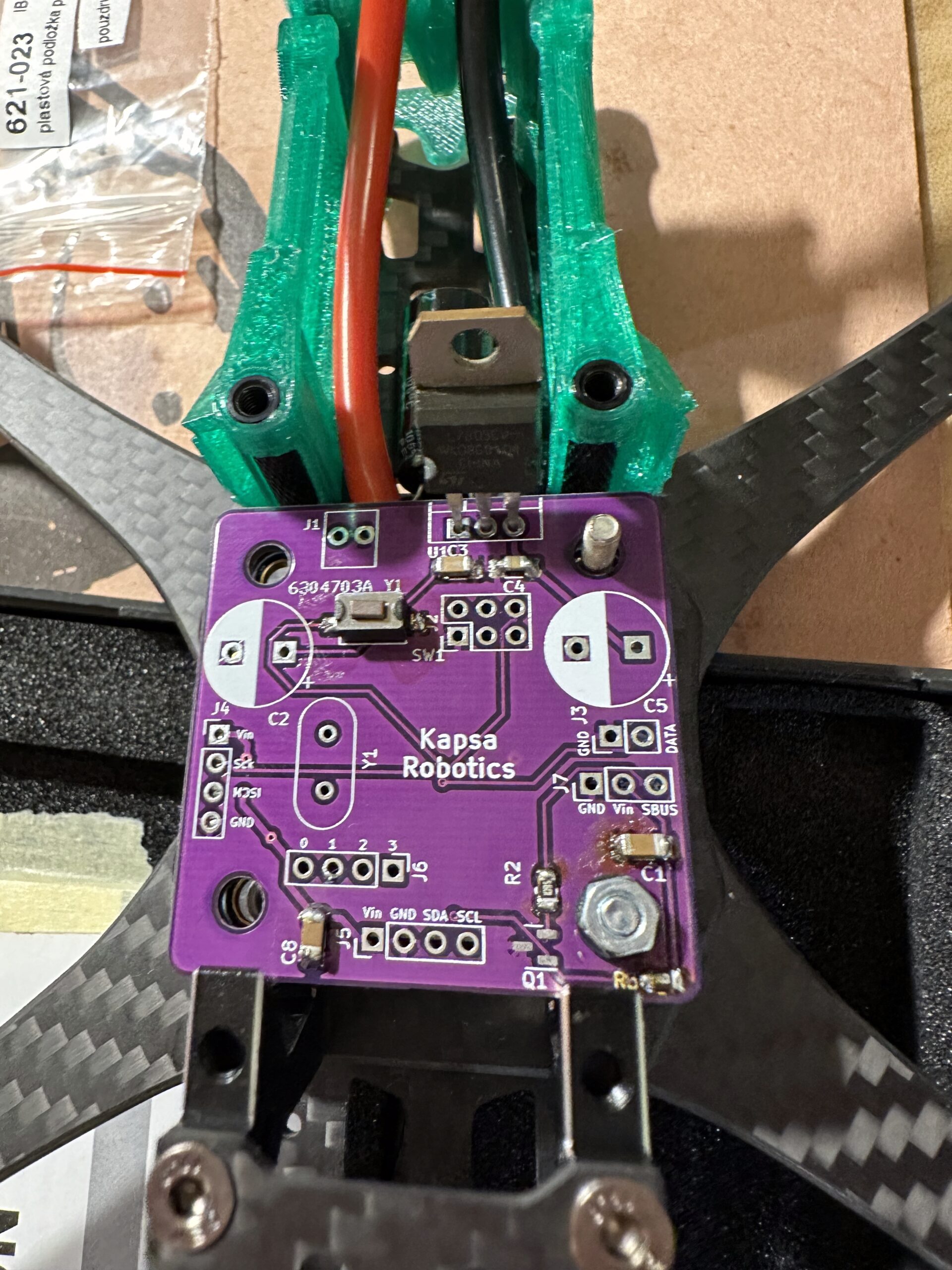 Detail fialové řídicí desky „Kapsa Robotics" na rámu dronu se zelenými 3D tisknutými díly a dráty.