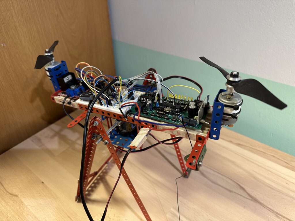 Malá konstrukce houpačky z Merkuru se dvěma vrtulemi umístěnými na červeném kovovém rámu s viditelnými elektronickými součástmi a elektroinstalací.