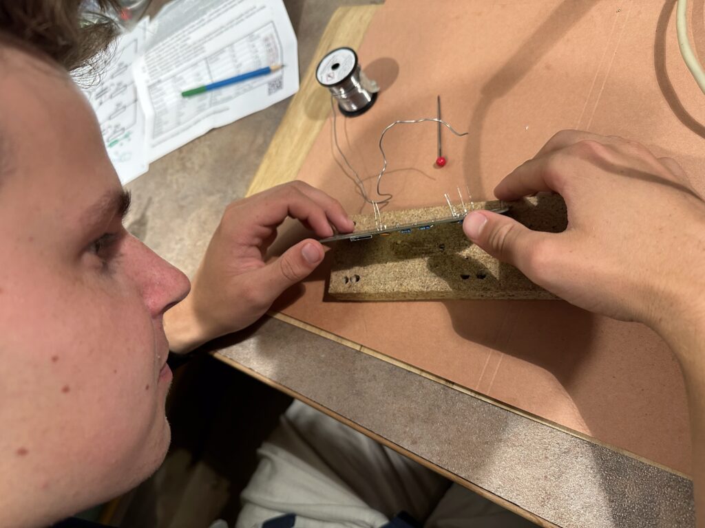 Student drží plošný spoj, do kterého vkládá drátové rezistory k připájení.