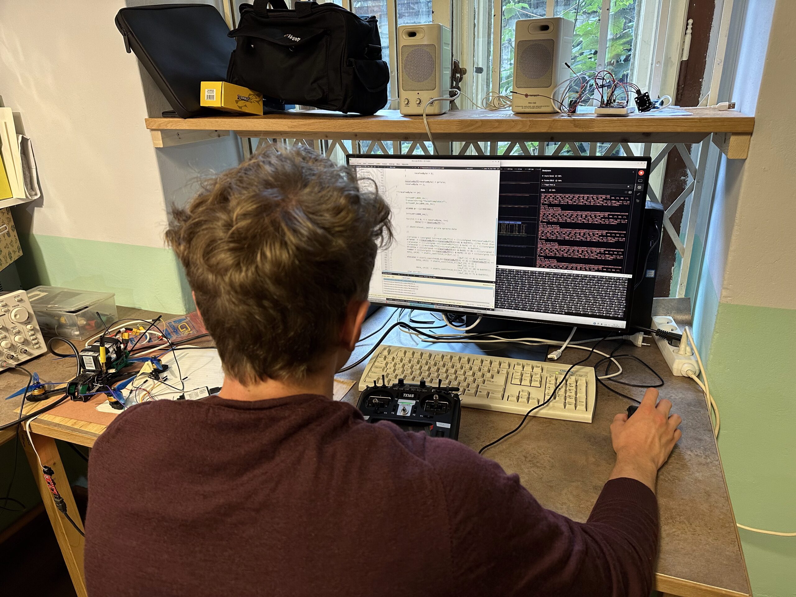 Student u monitoru zobrazujícího kód a grafy logického analyzátoru, před ním na stole modelářská vysílačka.