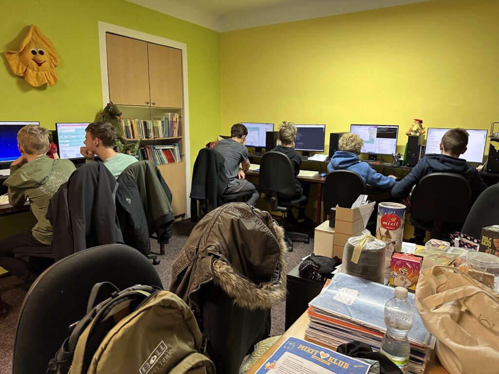 Děti a studenti při programování v učebně Klubu KAPSA se žlutými stěnami.