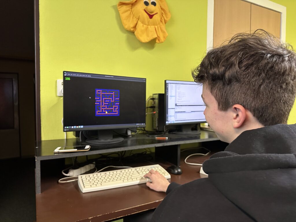 Kluk hrající Pac-Mana na počítači v místnosti se zelenou stěnou a žlutým sluncem.