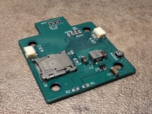 Zelená deska tištěných spojů s napájenými elektronickými součástkami, slotem na SD kartu a popsanými vývody.