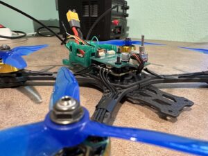 Detail modré vrtule dronu připojené k zelené desce tištěných spojů s viditelným zapojením.