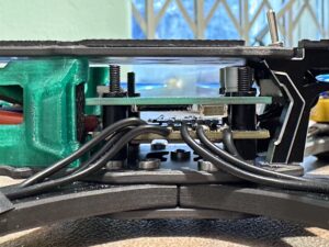 Detail sestavy elektronických desek v utrobách rámu dronu s čenými kabely, zeleným plastovým krytem, kovovými díly a karbonovým rámem.