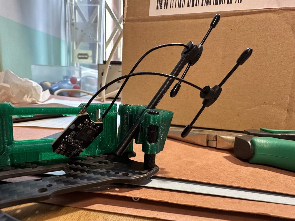 Zelený 3D tisknutý rám dronu s přichycenou deskou tištěných spojů, černými dráty a anténami.