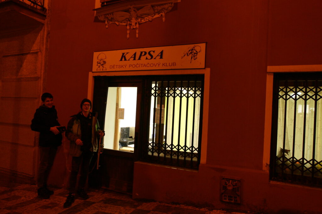 Dva kluci stojí před vchodem do Kapsy po setmění.