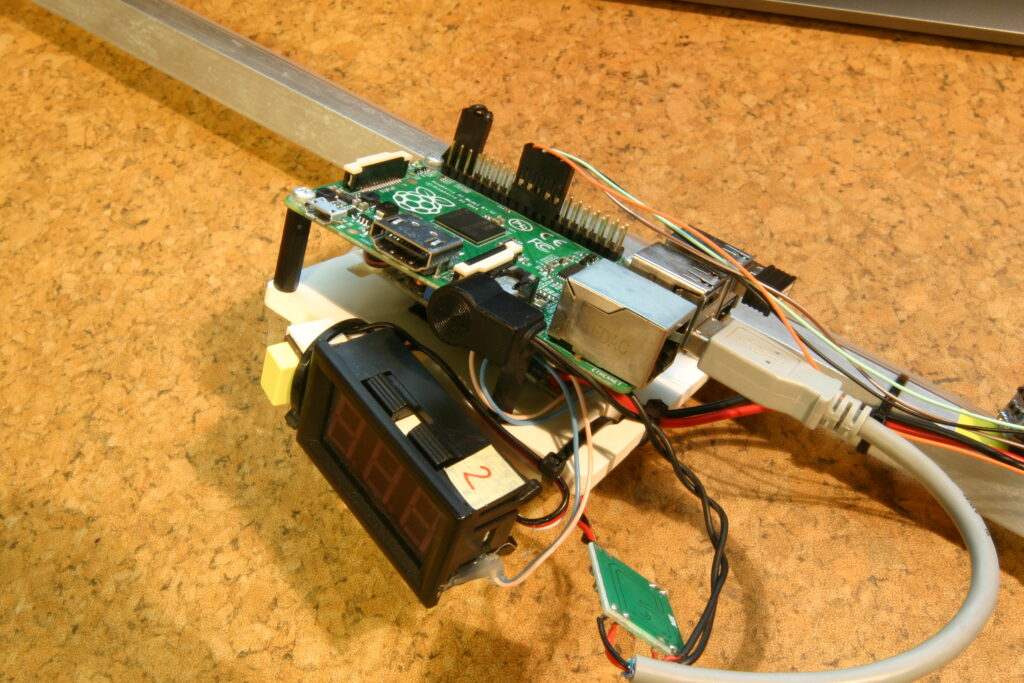 Elektronická montáž s deskou Raspberry Pi, digitální displej s "888", dráty, USB konektory a kovovou lištou na korkovém stp.