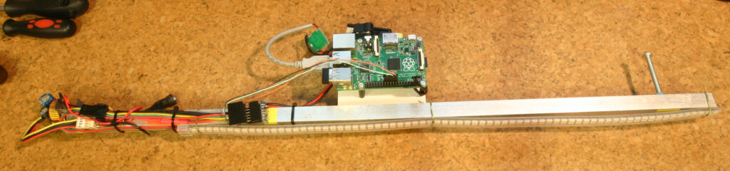 Raspberry Pi deska připojená k LED pásku a různé elektronické komponenty na korkovém povrchu.