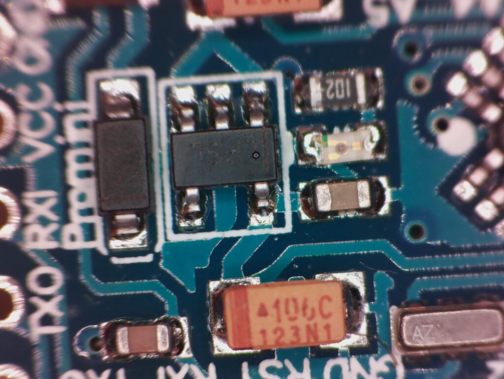 Mikroskopický pohled na modrý tištěný obvod s integrovaným obvodem s označením "LPSL," rezistory, kondenzátory a označenými elektrickými spoji.