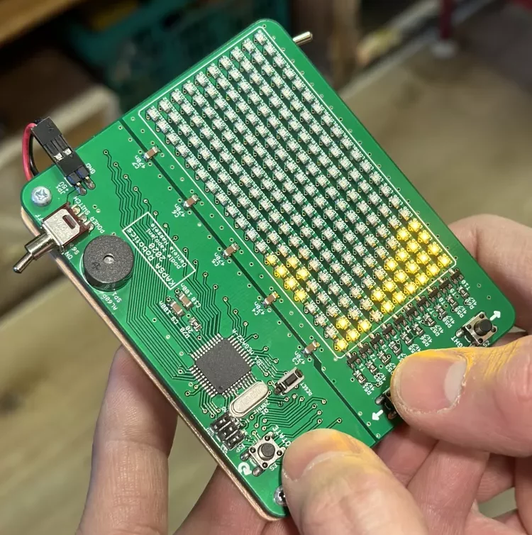 Ruce držící zelenou desku tištěných obvodů s osvětlenou LED mřížkou a elektronickými součástmi.