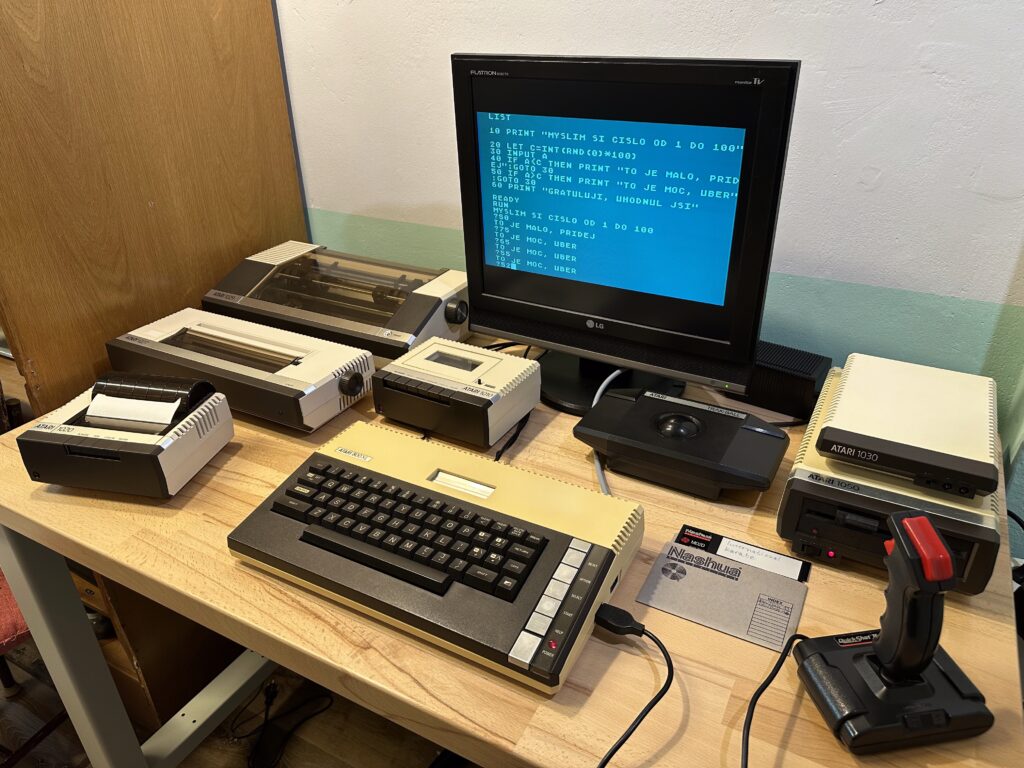 Retro počítačová sestava počítače Atario 800 XL, za ním LG monitor s BASICem, Atari 1030 modem, disketová jednotka, tři tiskárny, joystick a magnetofon.