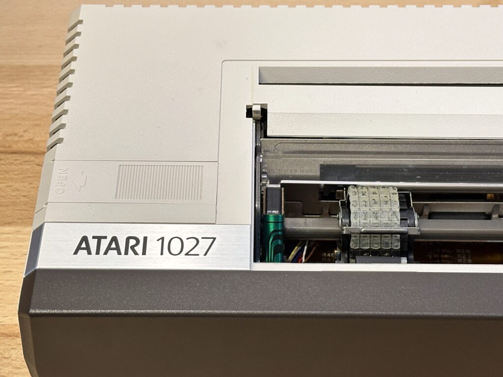 Detail na tiskovou hlavu retro tiskárny Atari 1027 s otevřeným krytem a viditelnými vnitřními součástkami.